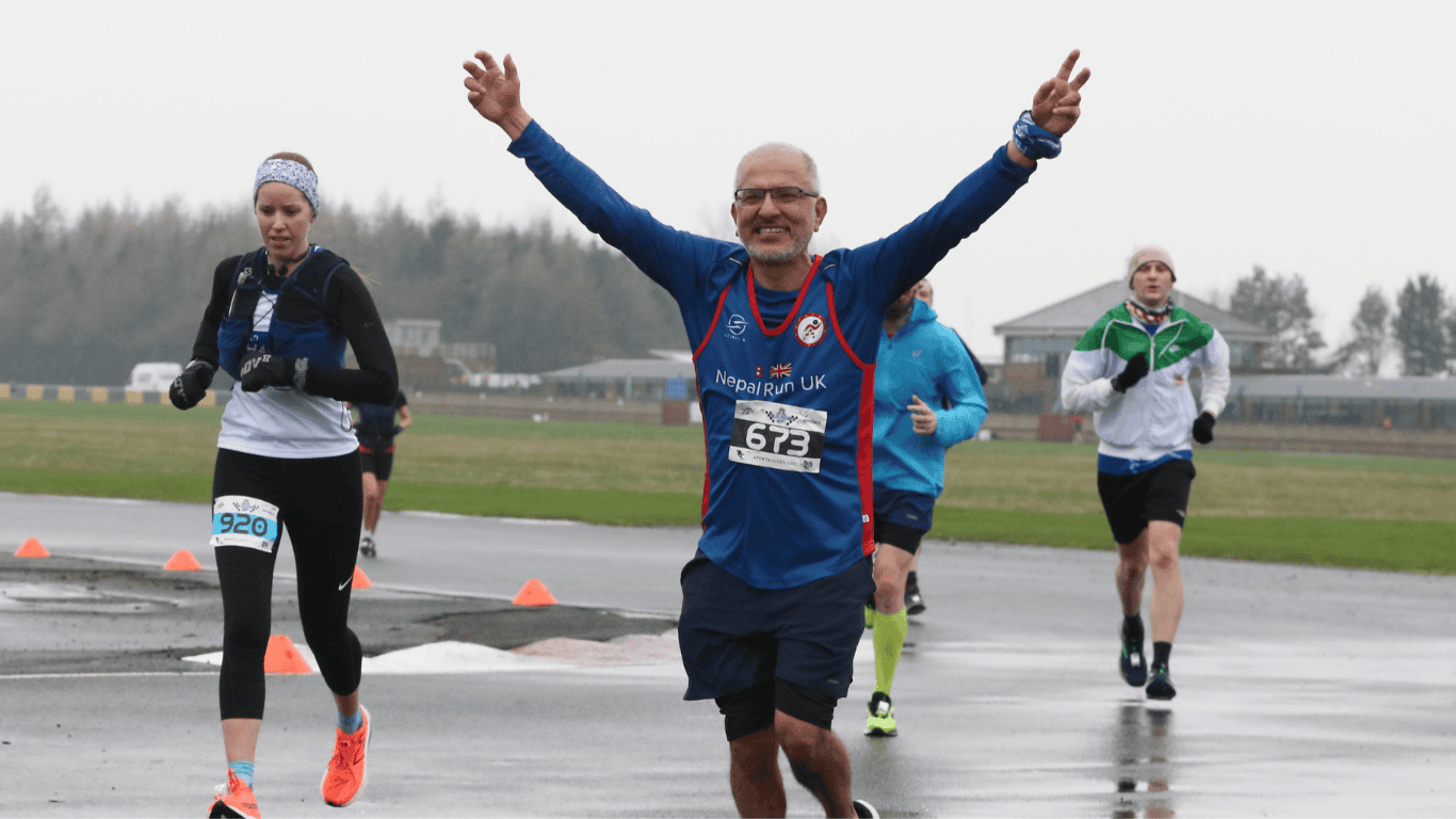 Runner on a motor circuit focusing on a man running with his arms in the air, triumphantly.