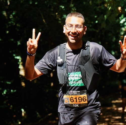 Man smiling and making peace signs with his hands as he runs through the forest.