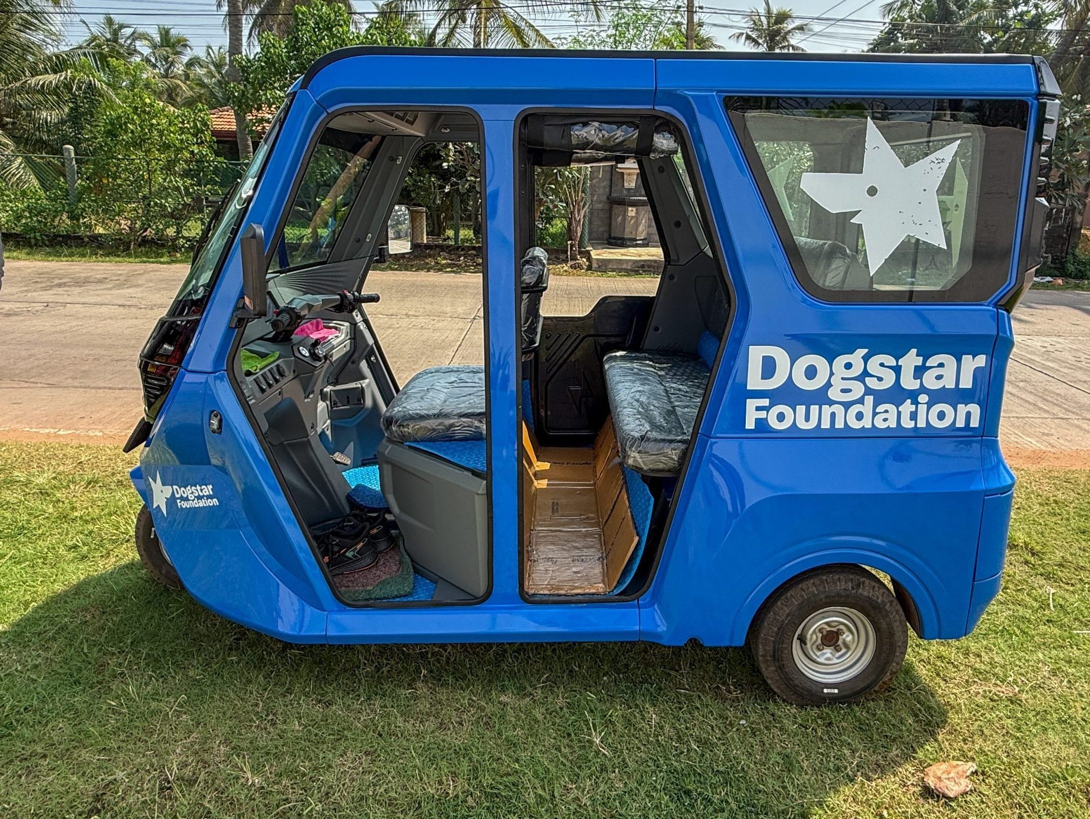 A side view of one of Dogstar's electric tuk-tuks. The vehicle is blue and Dogstar's logo is printed on the window.